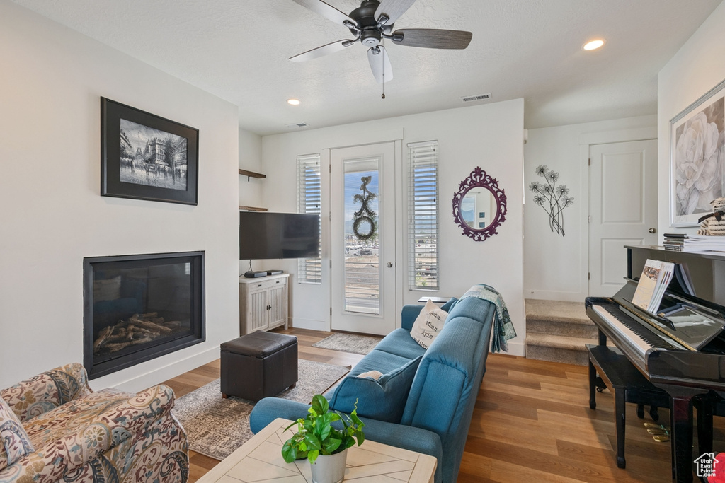 Living room featuring a glass covered fireplace, light wood finished floors, a ceiling fan, recessed lighting, and baseboards