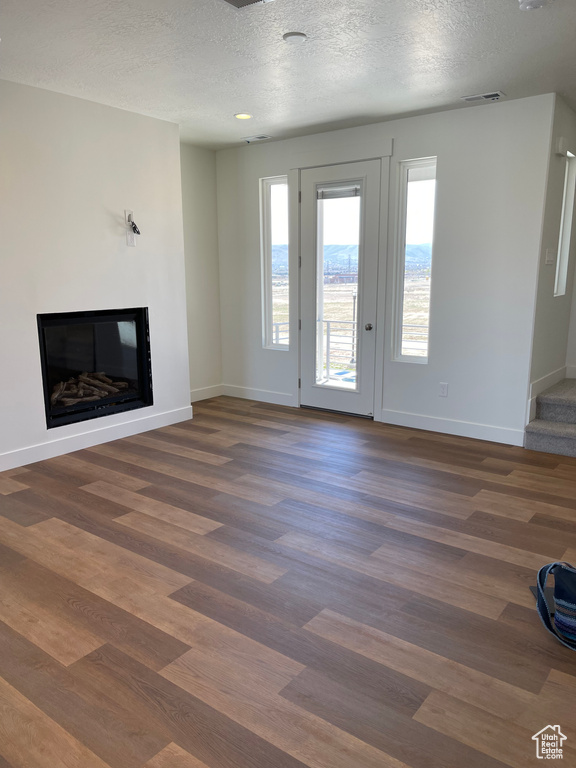 Unfurnished living room featuring a glass covered fireplace, baseboards, dark wood-style flooring, and a textured ceiling