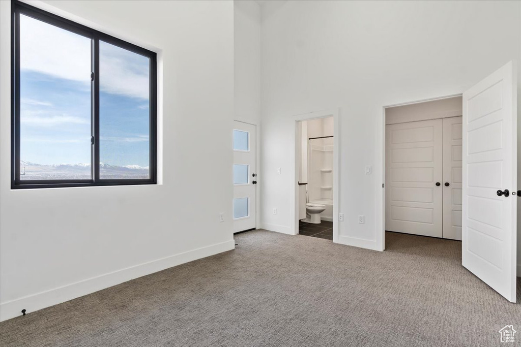 Unfurnished bedroom featuring carpet floors, baseboards, ensuite bathroom, and multiple windows