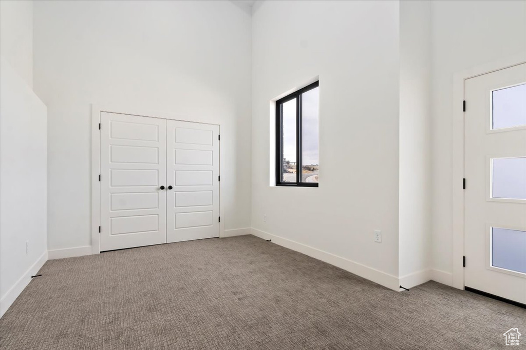 Unfurnished bedroom with baseboards, carpet, a high ceiling, and a closet