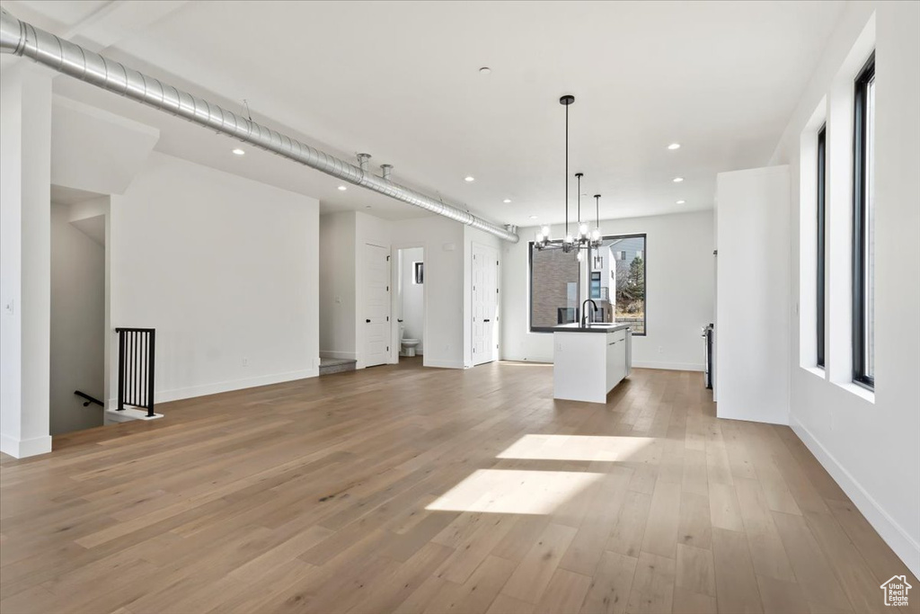 Unfurnished living room with baseboards, light wood-type flooring, recessed lighting, a sink, and a notable chandelier