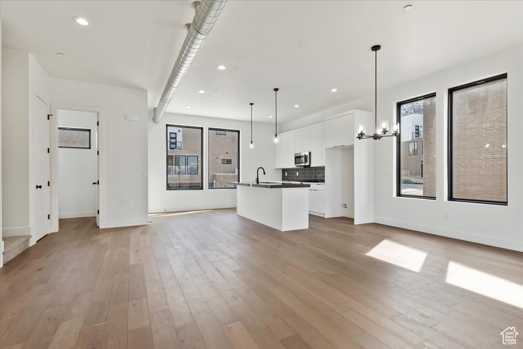 Unfurnished living room featuring a healthy amount of sunlight, light wood finished floors, and a chandelier