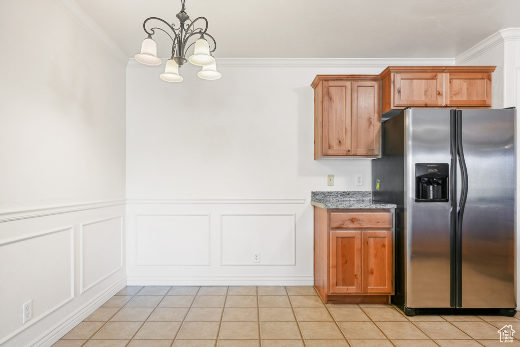 Kitchen featuring an inviting chandelier, stainless steel fridge, light stone counters, light tile patterned floors, and ornamental molding