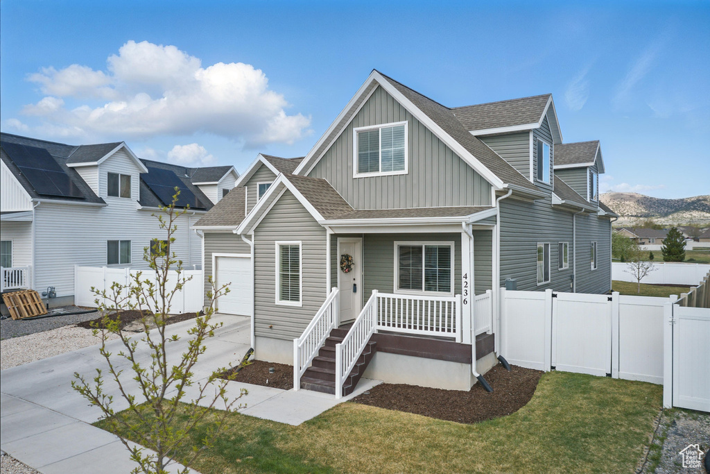 View of front facade with a porch, board and batten siding, driveway, fence, and a shingled roof