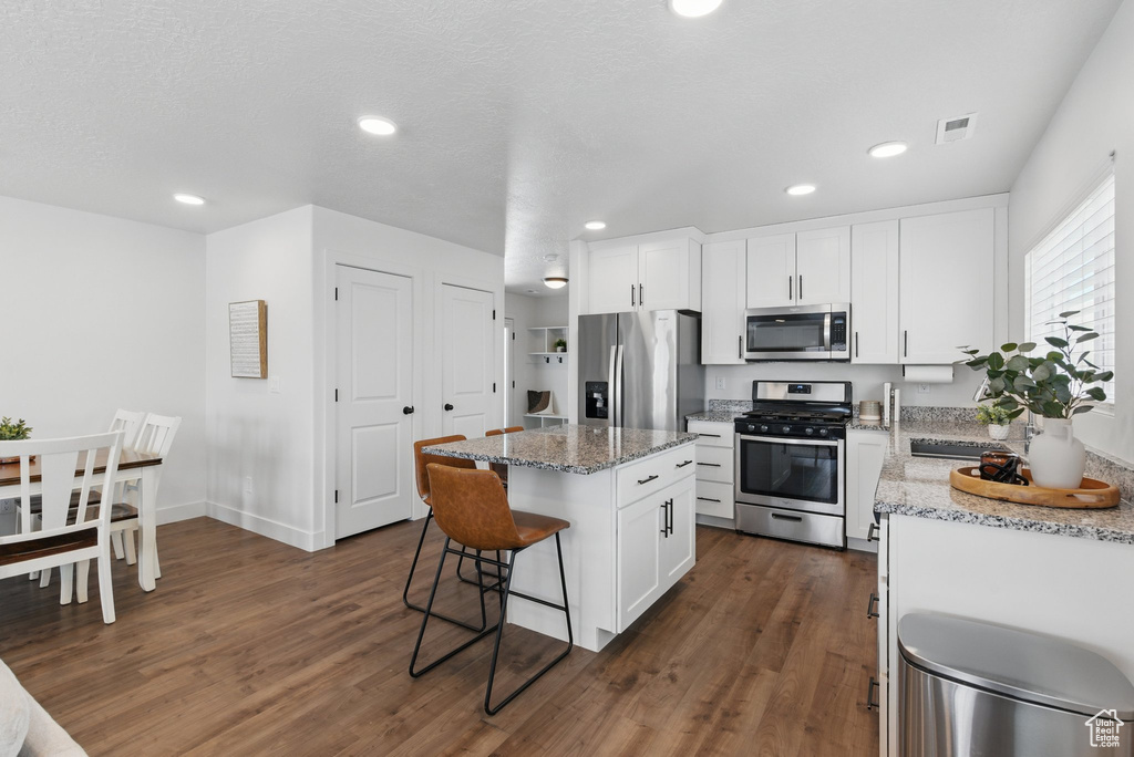 Kitchen featuring dark wood-style flooring, a kitchen island, a breakfast bar area, white cabinetry, and appliances with stainless steel finishes