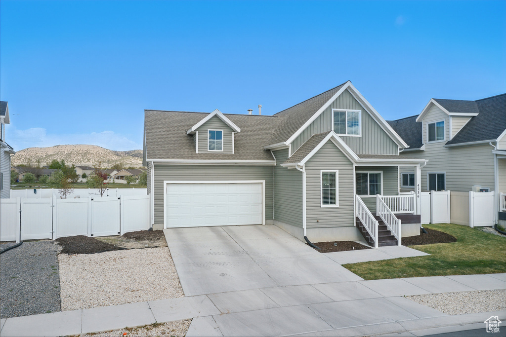 View of front facade with board and batten siding, fence, driveway, and roof with shingles
