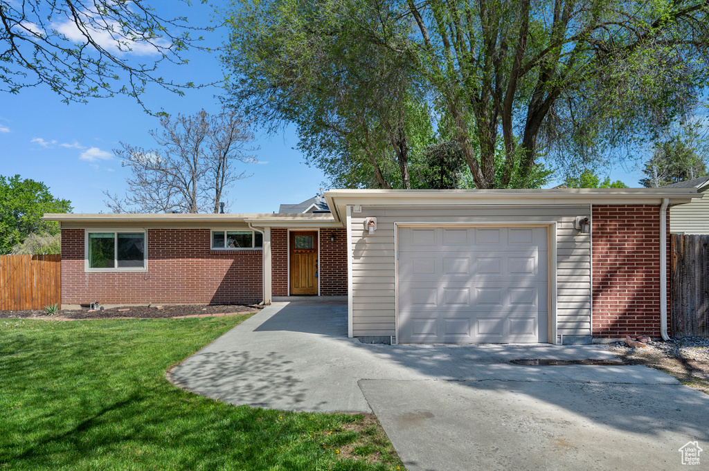 Ranch-style home featuring fence, an attached garage, a front lawn, and brick siding