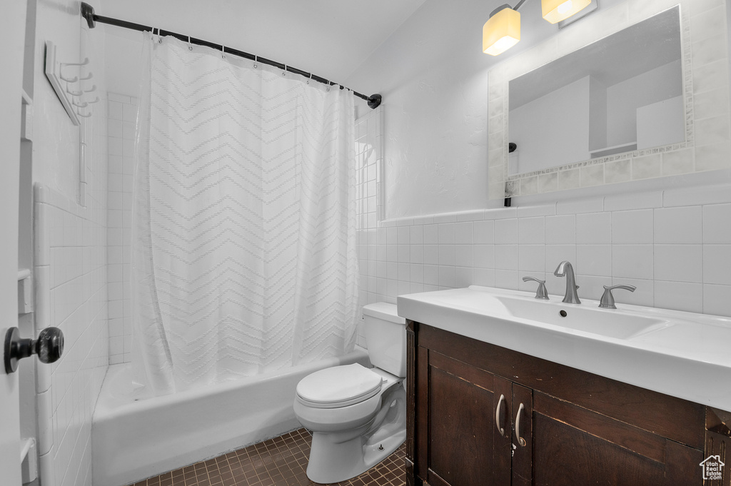 Full bathroom with vanity, toilet, tile patterned floors, shower / bathtub combination with curtain, and tile walls
