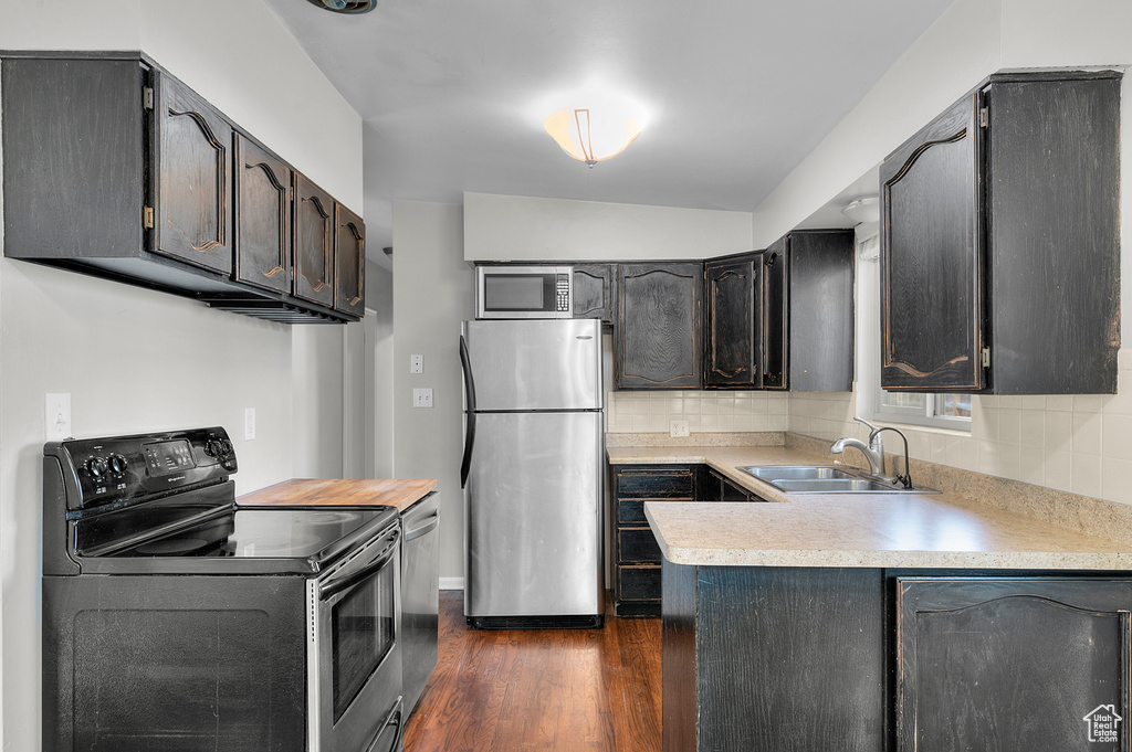 Kitchen with decorative backsplash, dark wood-type flooring, light countertops, a sink, and appliances with stainless steel finishes