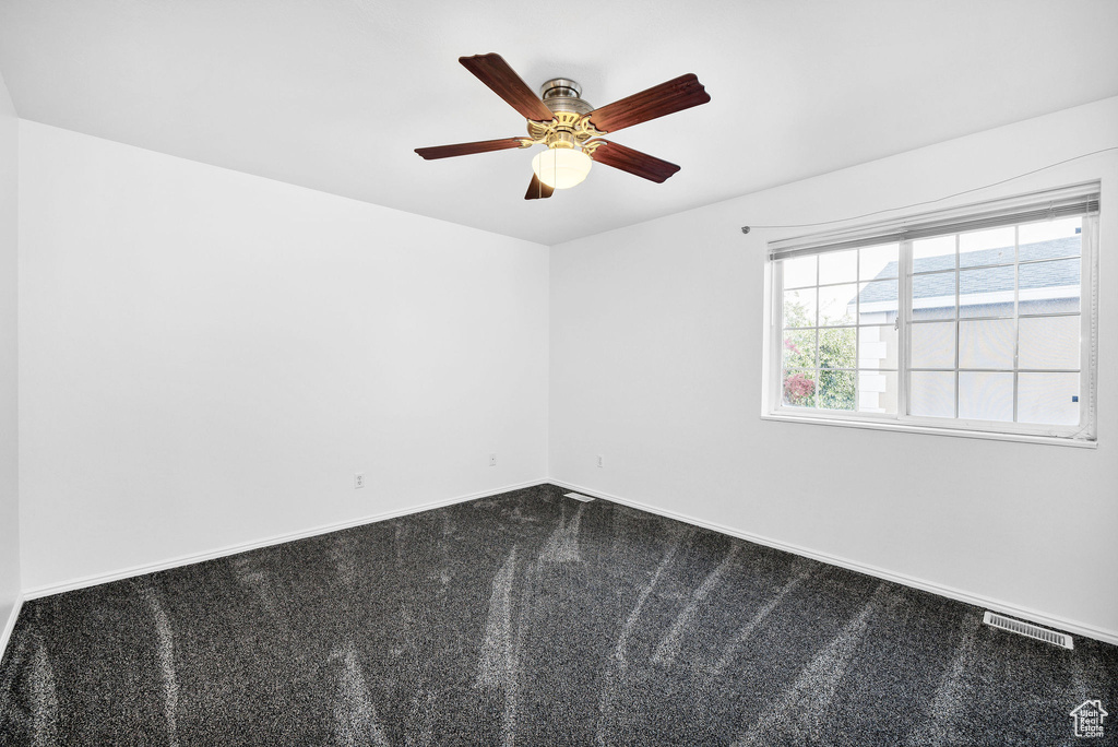 Unfurnished room featuring a ceiling fan, baseboards, visible vents, and dark colored carpet