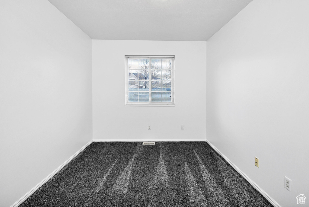 Unfurnished room with dark carpet, baseboards, and visible vents