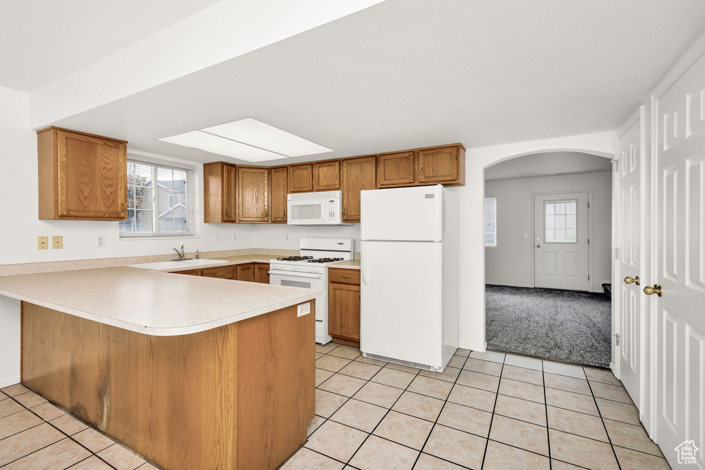 Kitchen featuring arched walkways, brown cabinets, light tile patterned floors, a peninsula, and white appliances