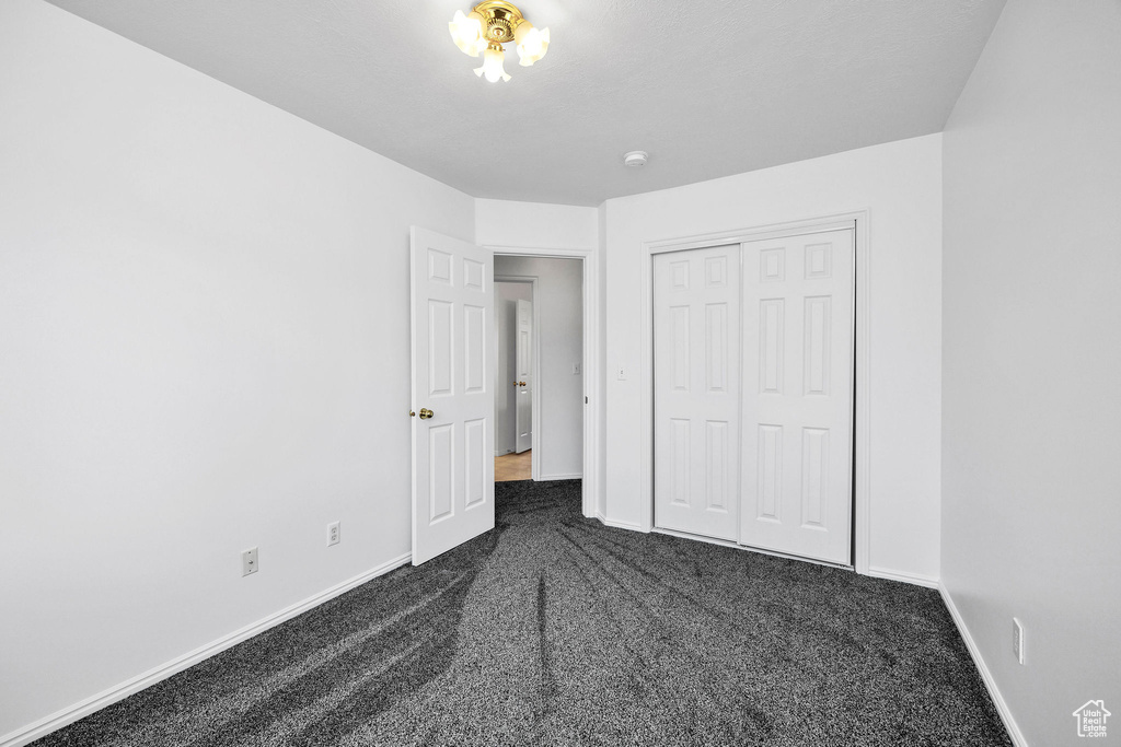Unfurnished bedroom featuring baseboards, a closet, and dark colored carpet
