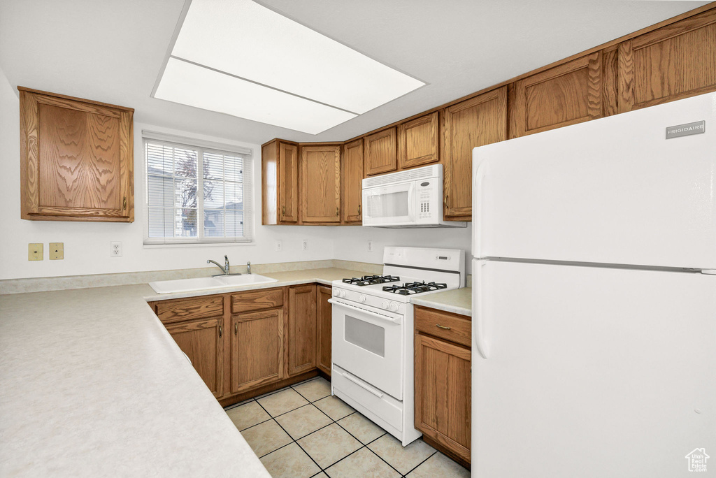 Kitchen featuring white appliances, brown cabinetry, a sink, and light countertops