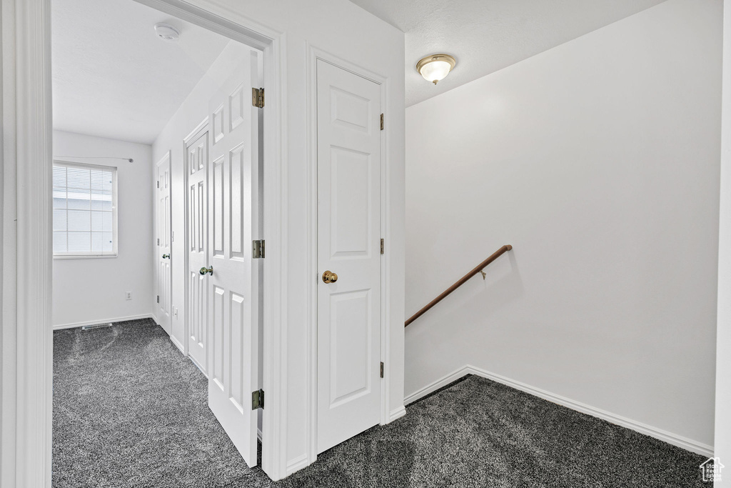 Hallway featuring baseboards, an upstairs landing, and dark carpet