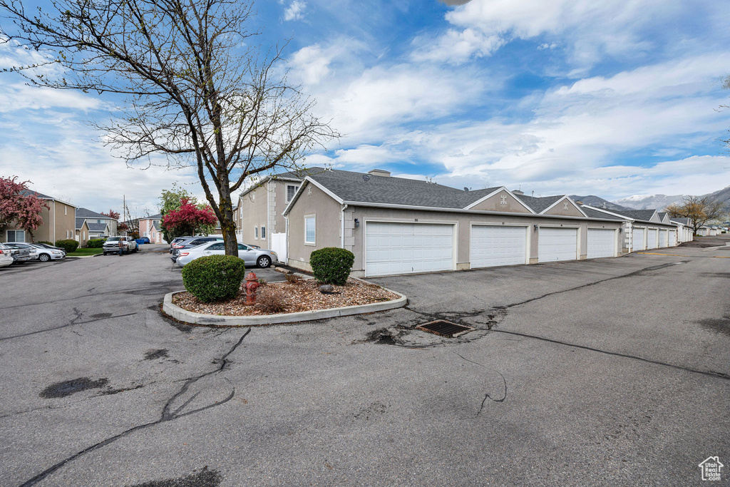 View of side of home featuring a residential view, stucco siding, roof with shingles, and community garages
