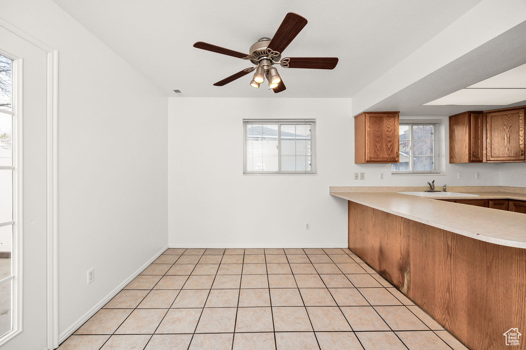 Kitchen featuring brown cabinetry, light tile patterned flooring, baseboards, light countertops, and a sink