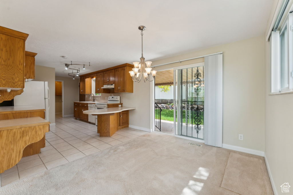 Kitchen featuring brown cabinets, an inviting chandelier, light countertops, a peninsula, and light tile patterned floors