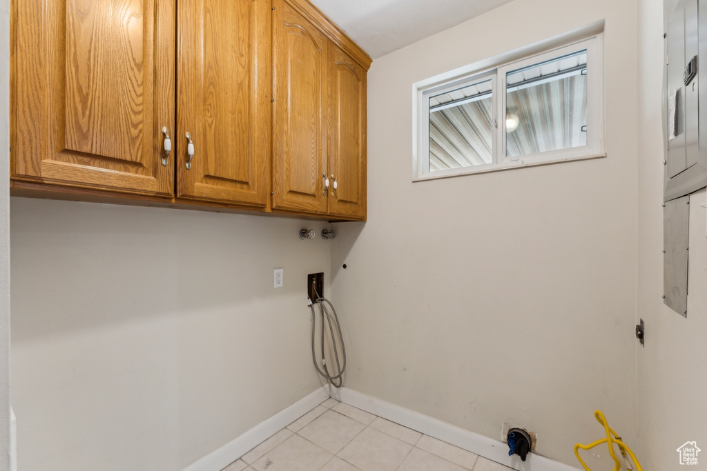 Clothes washing area featuring cabinet space, light tile patterned floors, baseboards, and washer hookup