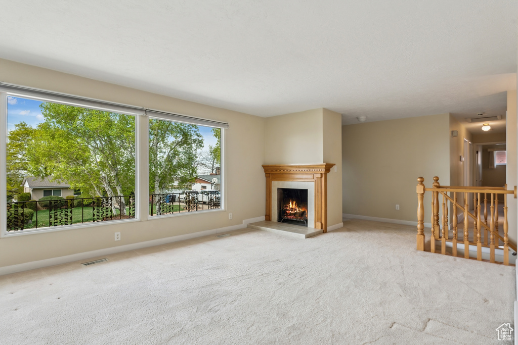 Unfurnished living room featuring baseboards, carpet, a lit fireplace, and visible vents