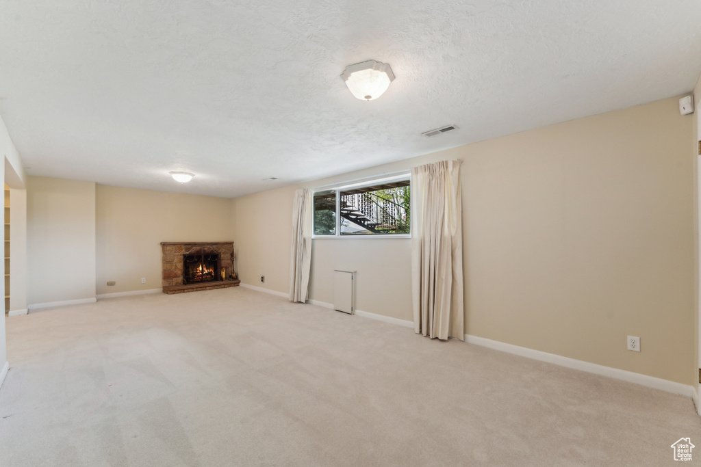 Unfurnished living room with baseboards, visible vents, light carpet, and a fireplace