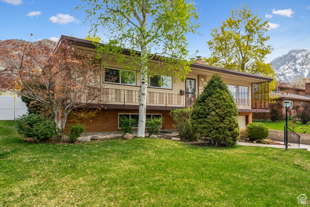 View of front facade with brick siding, fence, a mountain view, and a front yard