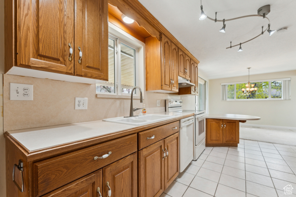 Kitchen with brown cabinetry, a peninsula, light tile patterned floors, a sink, and dishwasher