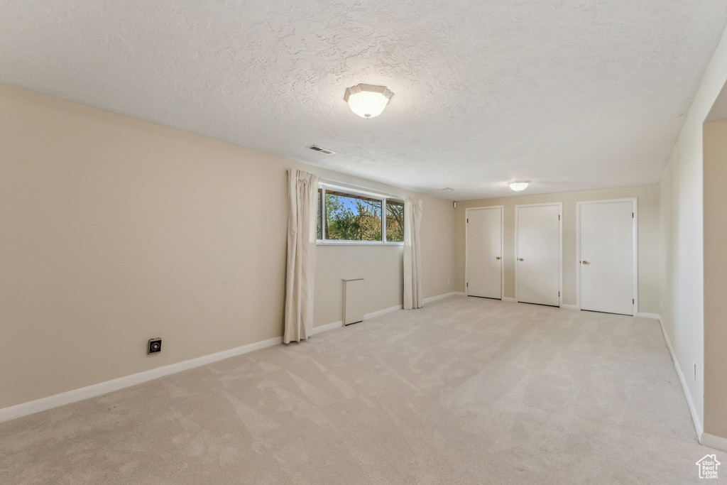 Unfurnished bedroom with visible vents, a textured ceiling, two closets, and light carpet