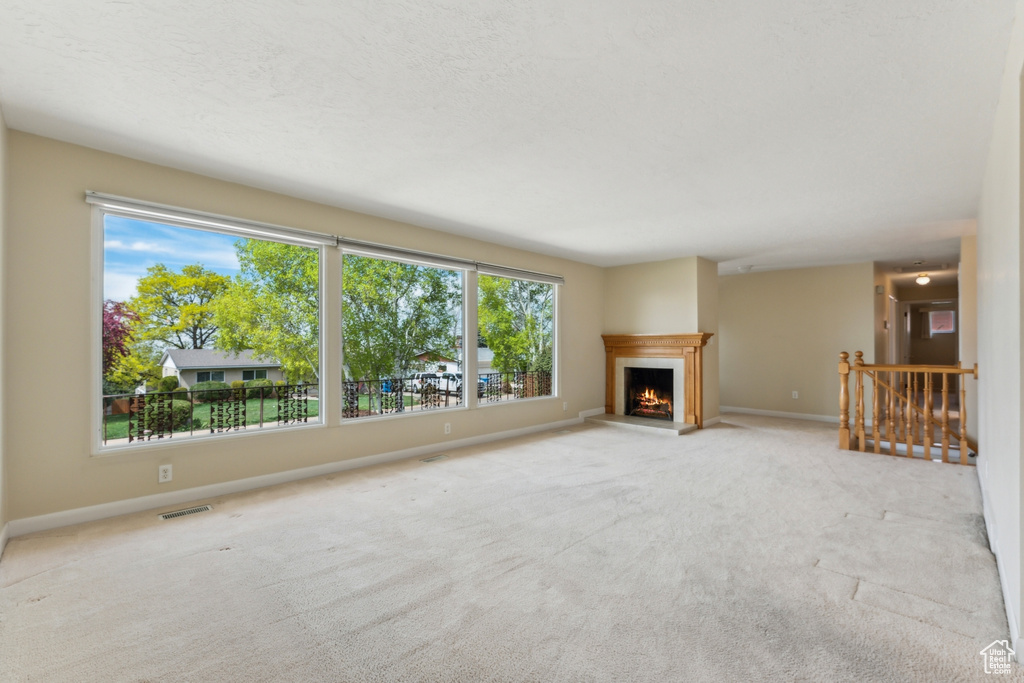 Unfurnished living room with carpet floors, a lit fireplace, baseboards, and visible vents