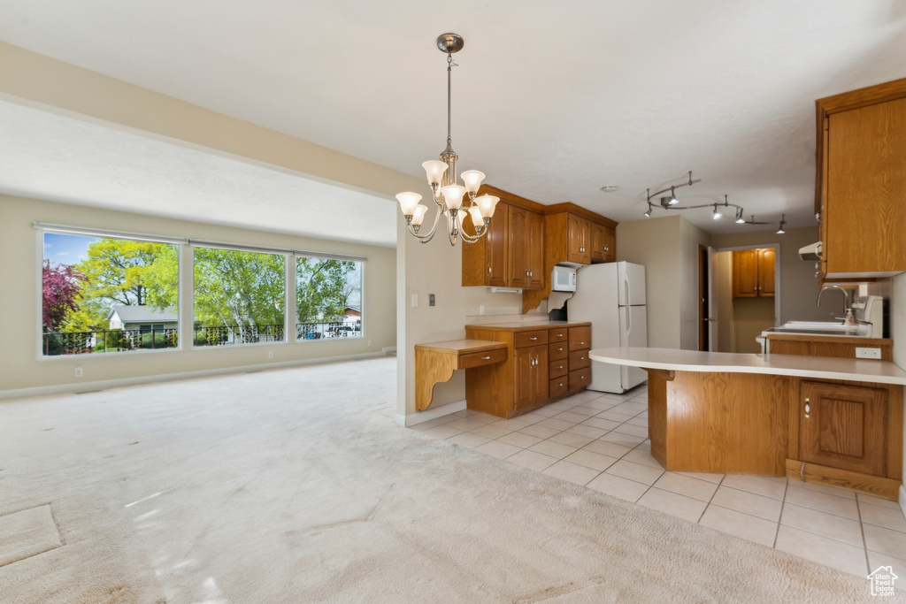 Kitchen featuring brown cabinets, a sink, light countertops, freestanding refrigerator, and an inviting chandelier