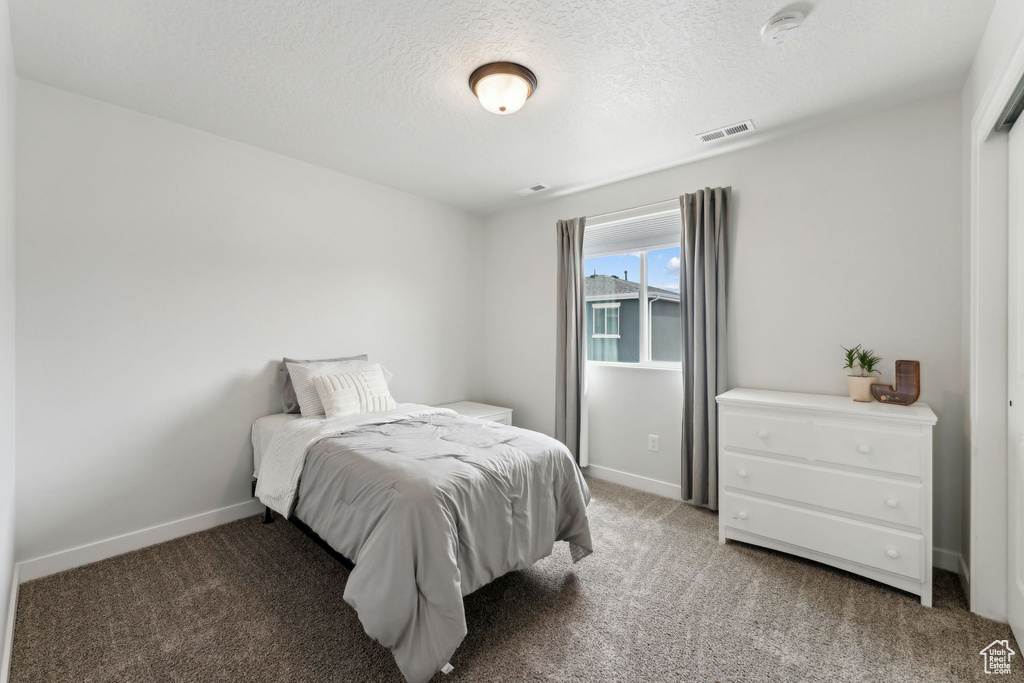 Bedroom with baseboards, light carpet, a textured ceiling, and visible vents