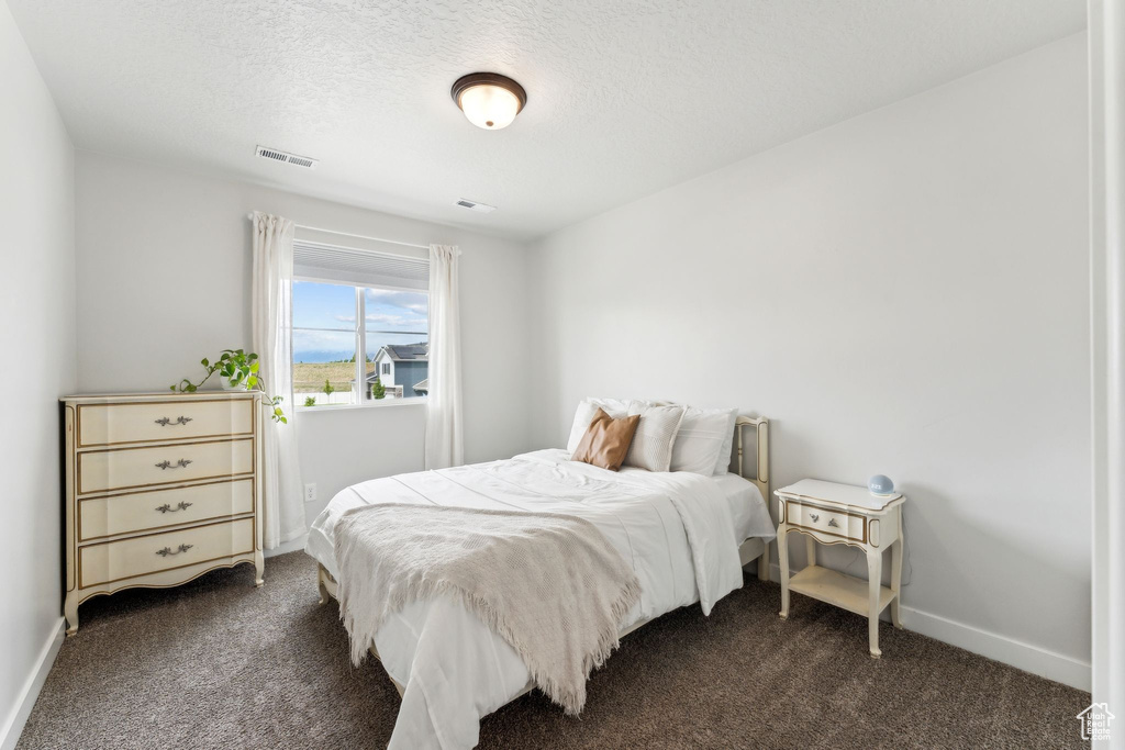 Bedroom featuring baseboards, dark carpet, a textured ceiling, and visible vents