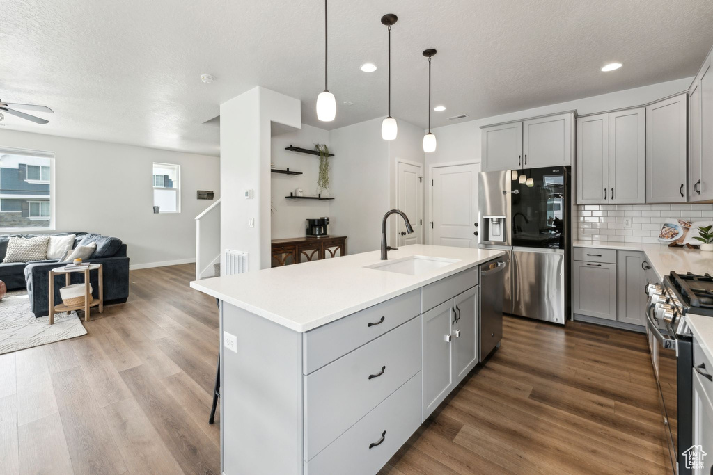 Kitchen featuring a sink, stainless steel appliances, open floor plan, wood finished floors, and gray cabinetry