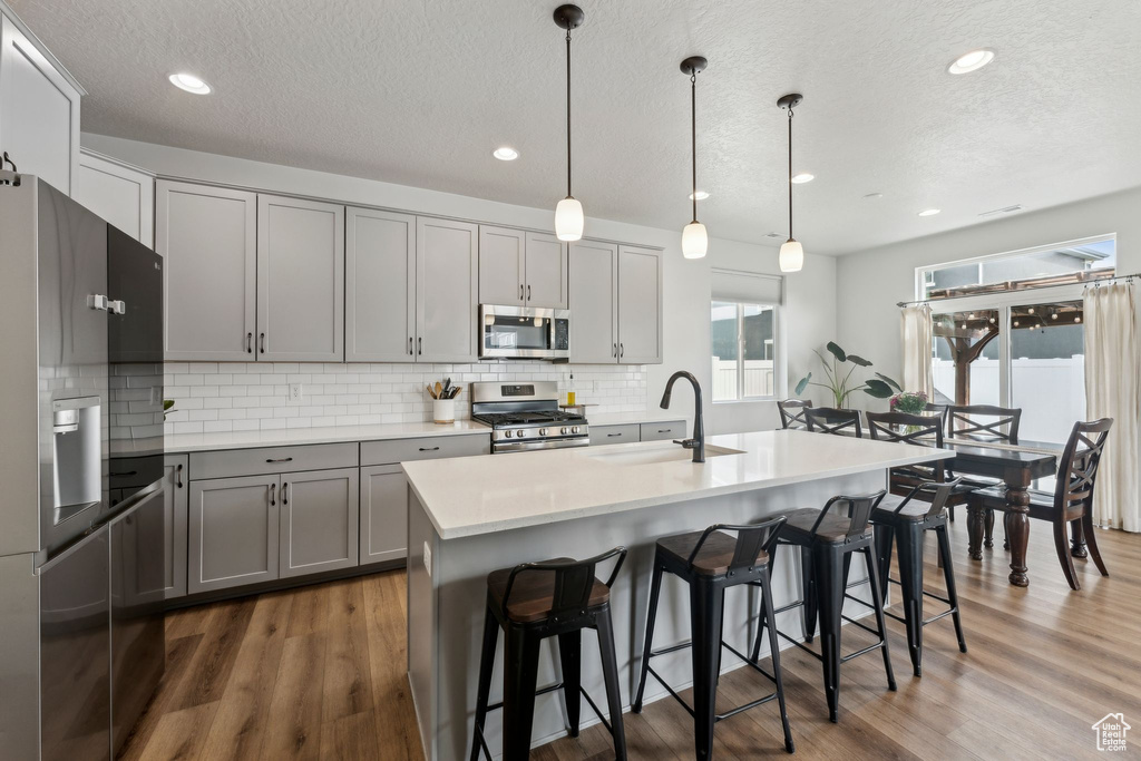 Kitchen with a sink, appliances with stainless steel finishes, gray cabinets, and tasteful backsplash