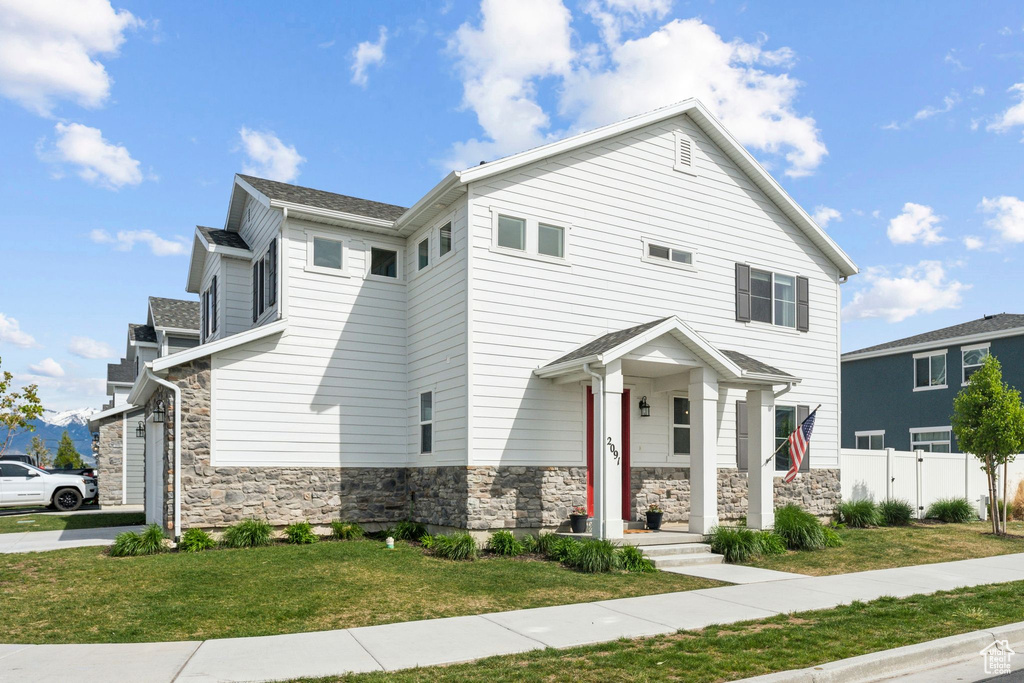 View of front of house featuring a front lawn, fence, and stone siding