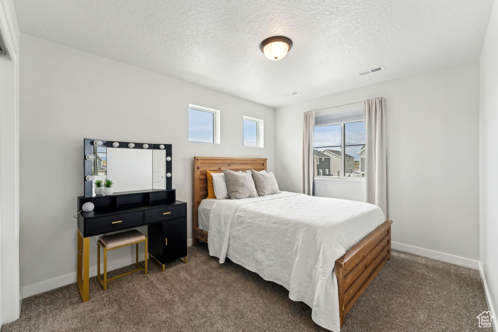 Bedroom featuring baseboards, dark colored carpet, a textured ceiling, and visible vents