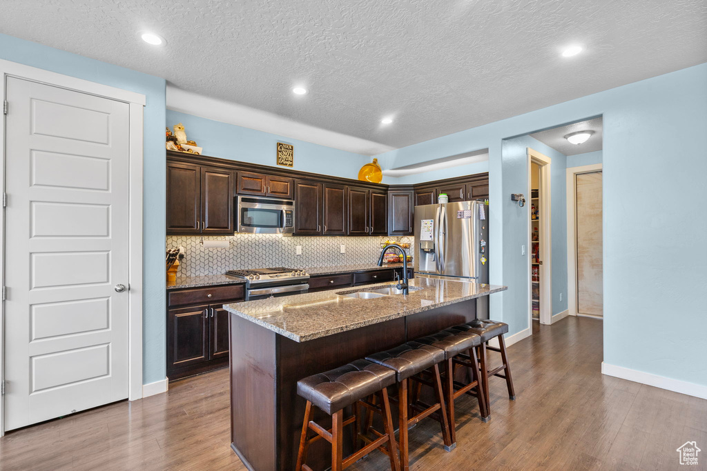 Kitchen with dark brown cabinets, appliances with stainless steel finishes, a sink, wood finished floors, and a kitchen bar