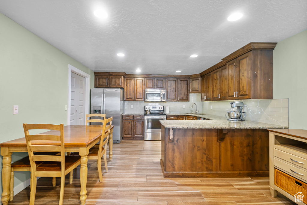 Kitchen featuring appliances with stainless steel finishes, a sink, a peninsula, light wood finished floors, and recessed lighting