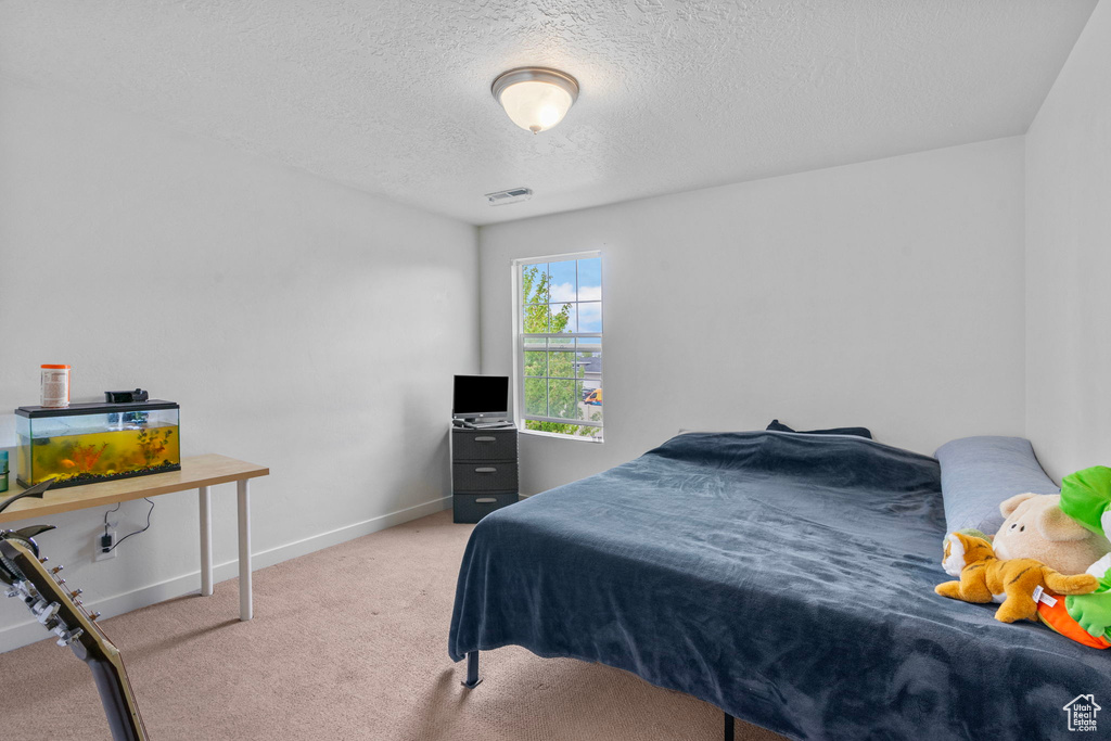 Bedroom with a textured ceiling, visible vents, baseboards, and carpet