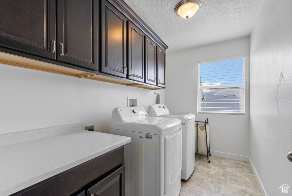 Clothes washing area with stone finish flooring, a textured ceiling, washing machine and clothes dryer, cabinet space, and baseboards