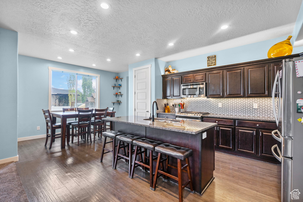 Kitchen featuring a breakfast bar, a sink, a kitchen island with sink, stainless steel appliances, and decorative backsplash