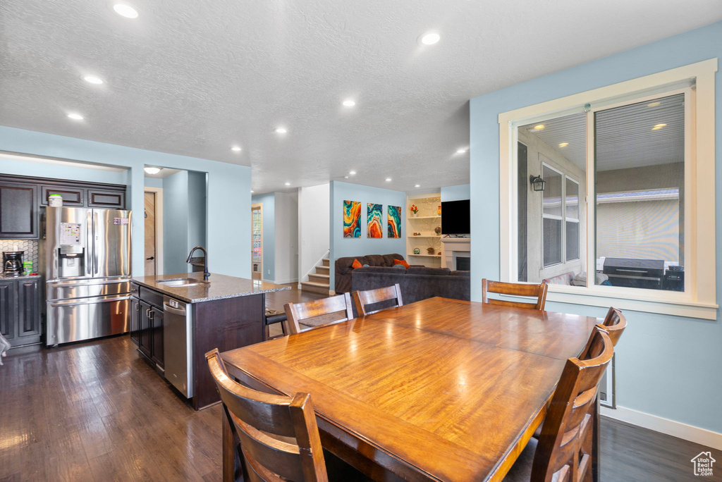 Dining area featuring a textured ceiling, a fireplace, stairway, recessed lighting, and dark wood-type flooring