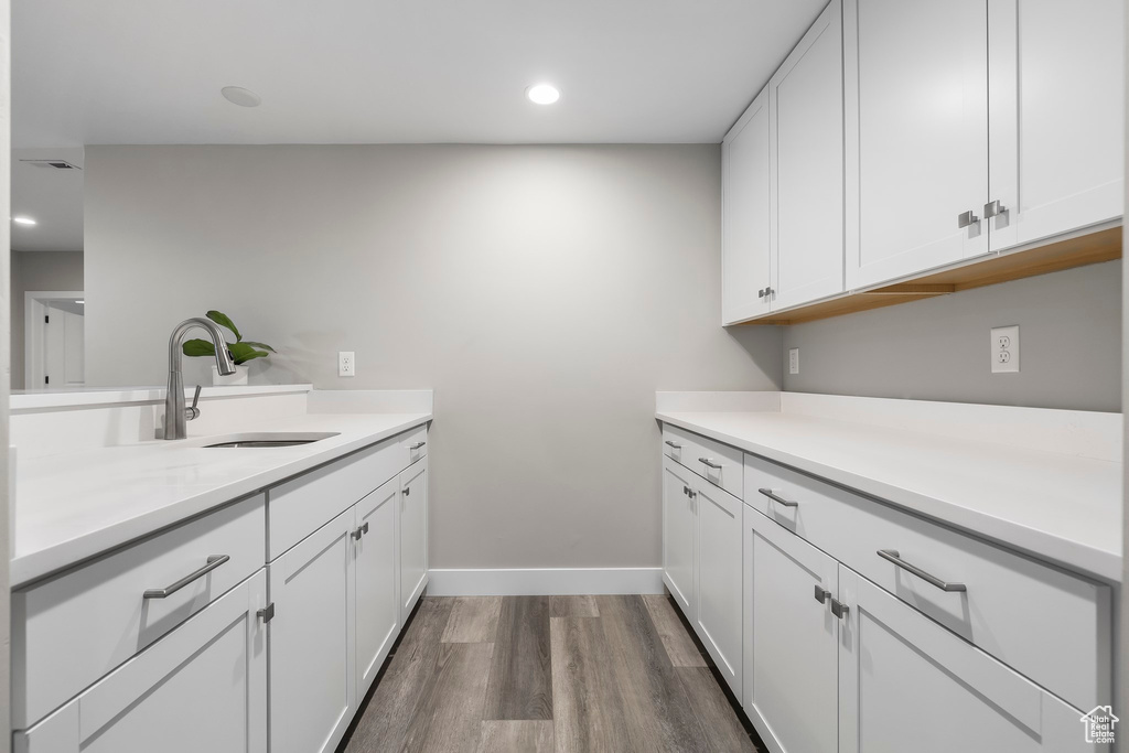 Interior space with dark wood finished floors, a sink, light countertops, baseboards, and white cabinetry