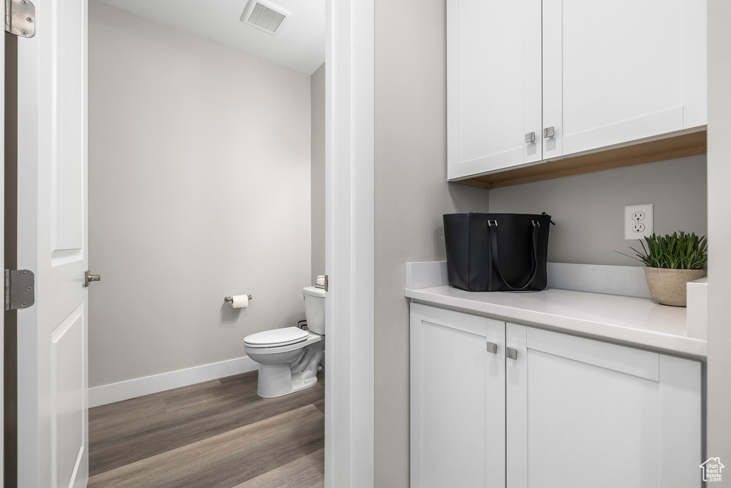 Half bath featuring toilet, baseboards, visible vents, and wood finished floors