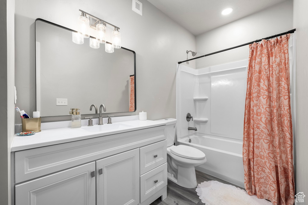 Bathroom featuring visible vents, shower / bath combo, wood finished floors, vanity, and toilet