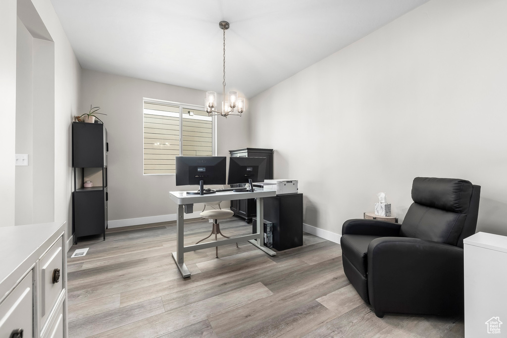 Home office featuring light wood-style floors, baseboards, vaulted ceiling, and a notable chandelier