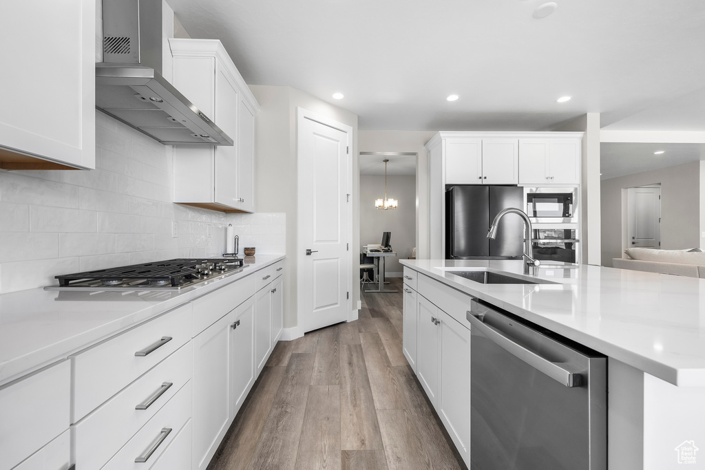 Kitchen with wall chimney range hood, appliances with stainless steel finishes, wood finished floors, light countertops, and a sink