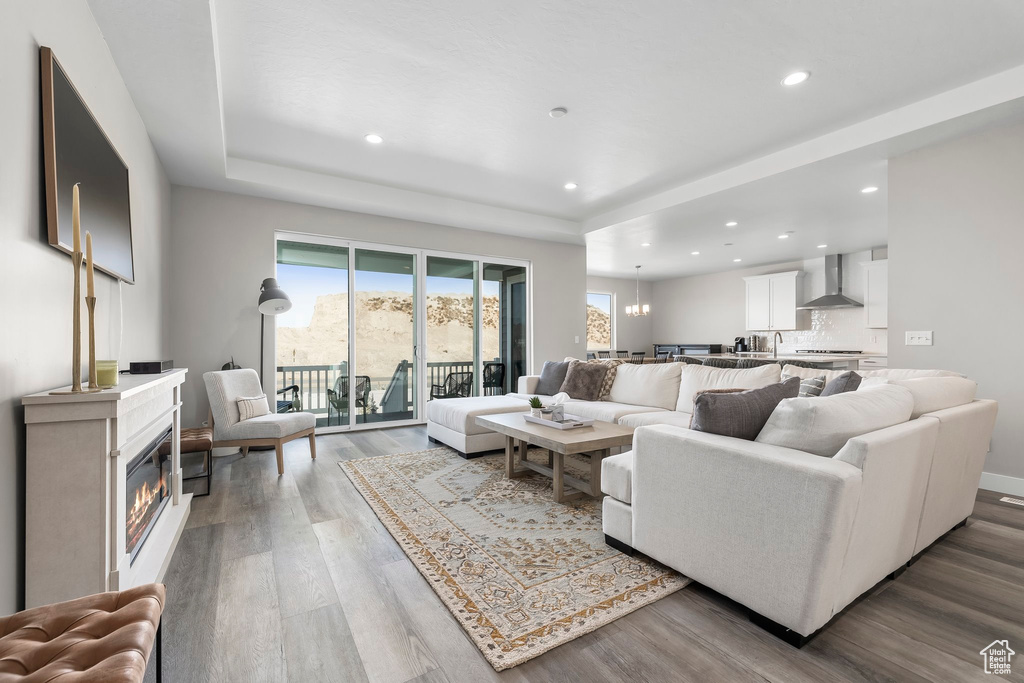 Living room featuring wood finished floors, a raised ceiling, baseboards, a glass covered fireplace, and recessed lighting