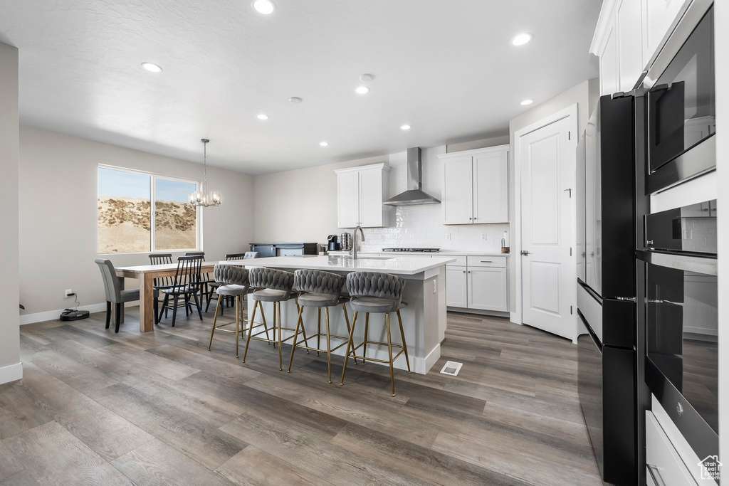 Kitchen featuring appliances with stainless steel finishes, a breakfast bar, recessed lighting, wall chimney exhaust hood, and an island with sink