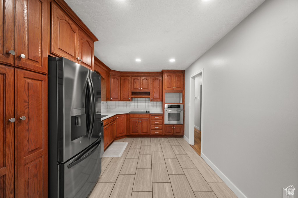 Kitchen with black appliances, tasteful backsplash, brown cabinets, light countertops, and recessed lighting